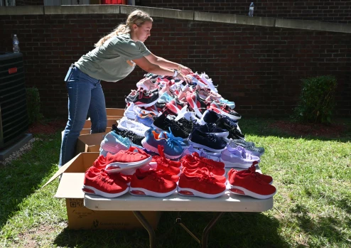A volunteer woman organizes dozens of pairs of new shoes on a table. The shoes will be given out to children at a community back-to-school event.